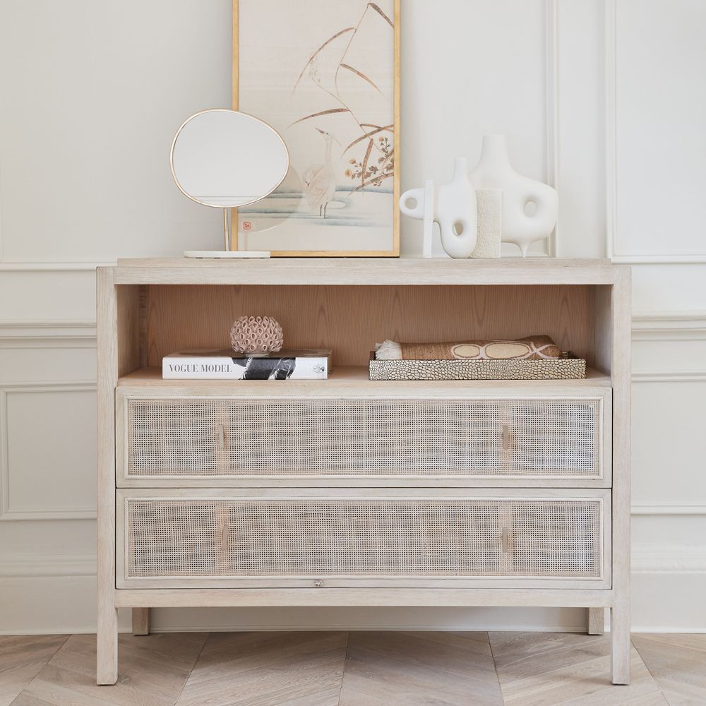 a rattan chest of drawers with accessories including vases, a mirror and art
