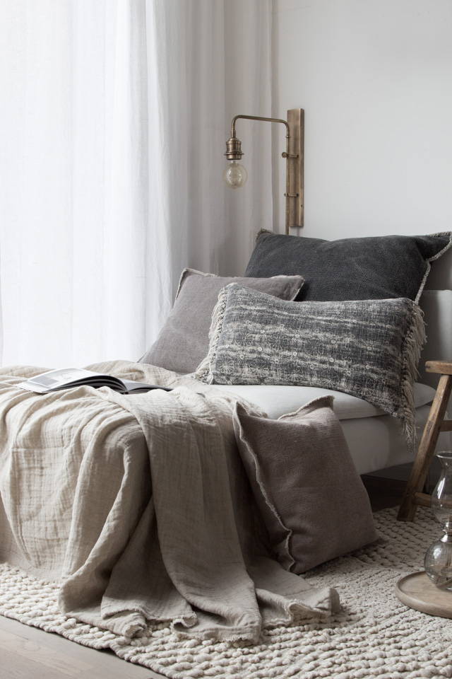 a cosy day bed draped with neutral-toned cushions and throws