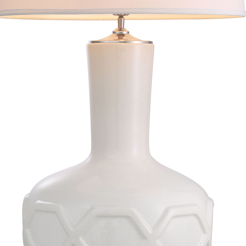 A stylish table lamp by Eichholtz with a white porcelain base featuring relief patterns, a crystal glass plinth and off-white fabric shade