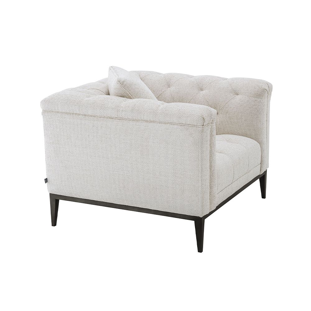 A luxurious armchair by Eichholtz with a square shaped design featuring a Lyssa off-white upholstery, deep buttoned stitching and a black gunmetal base