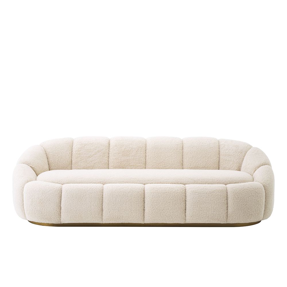 A luxurious sofa with a sumptuous boucle upholstery, wide fluting details, gorgeous curves and a beautiful brushed brass base