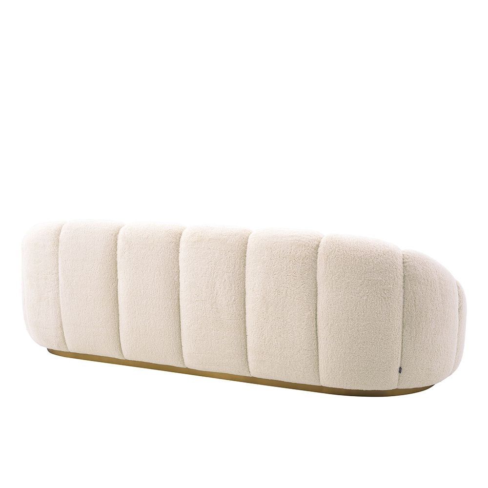 A luxurious sofa with a sumptuous boucle upholstery, wide fluting details, gorgeous curves and a beautiful brushed brass base