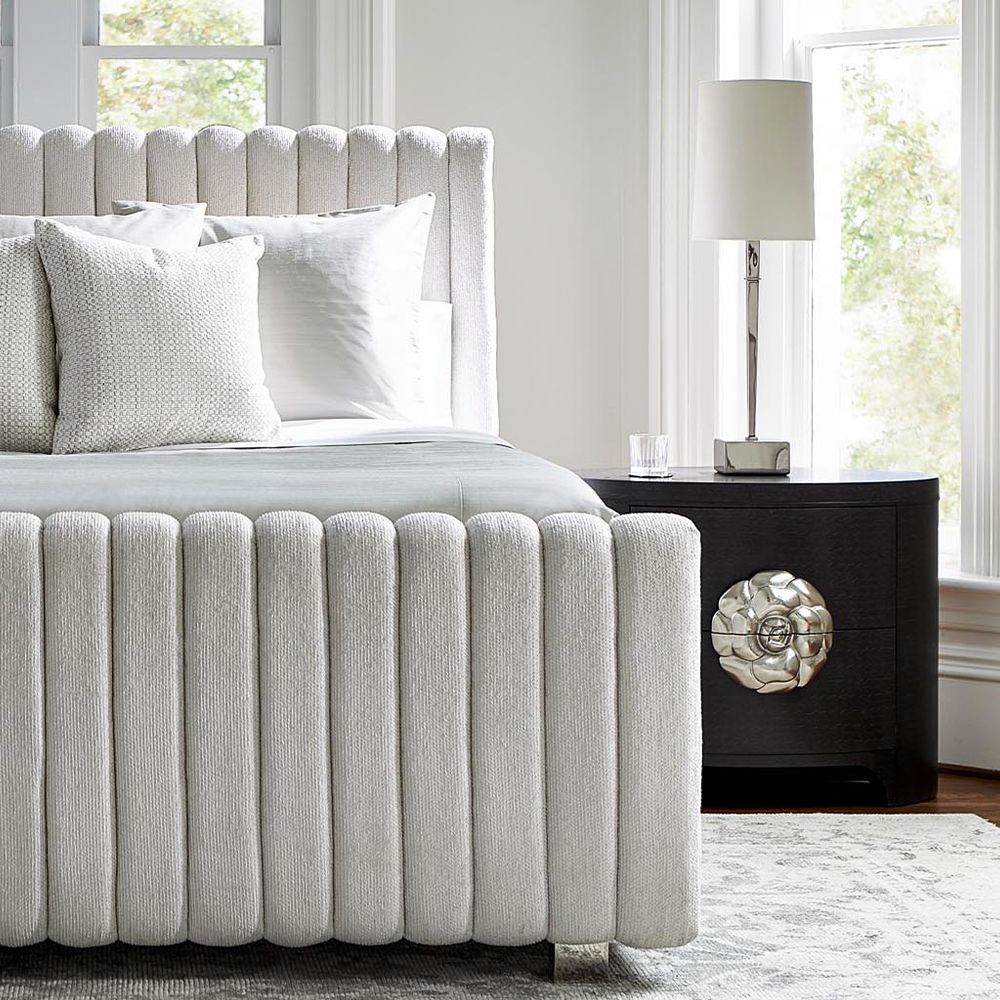 A sophisticated oval shaped two drawer bedside table with a silver aluminium flower hardware pull