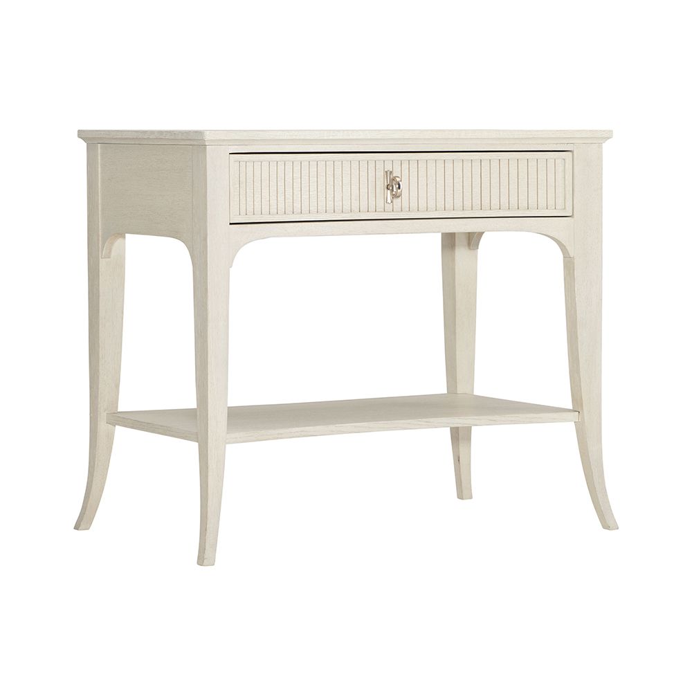 A sophisticated one-drawer bedside table with a concave shape, quartered white oak veneers, a Manor White finish and silver luster highlights