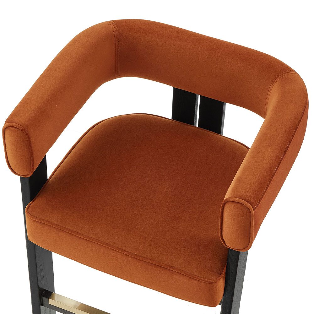 A luxury counter stool with a red and orange velvet upholstery and brass detailing