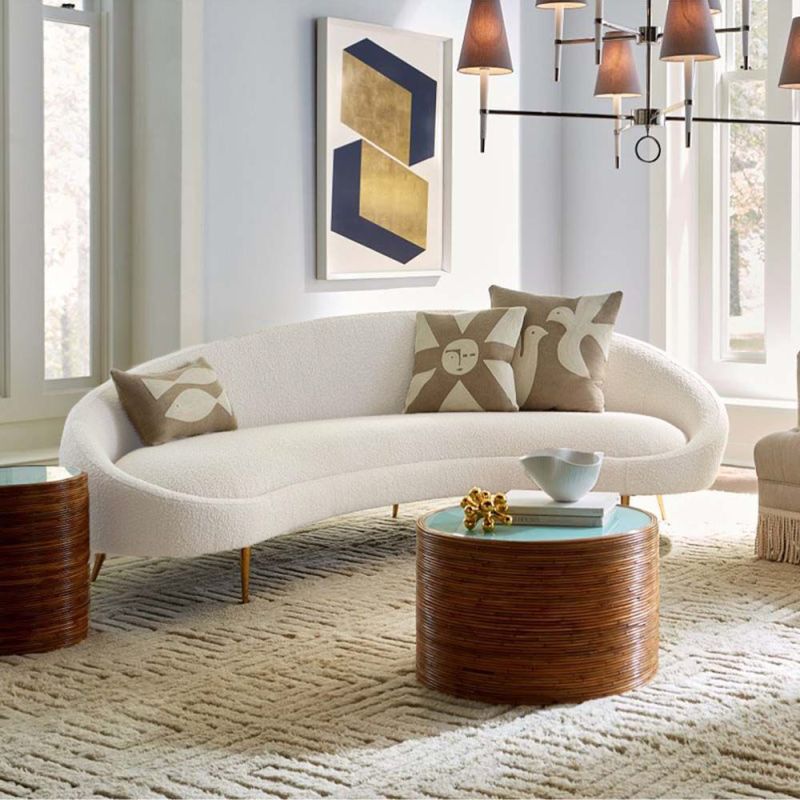 A curved sofa in an upholstered beige boucle fabric with brass legs.