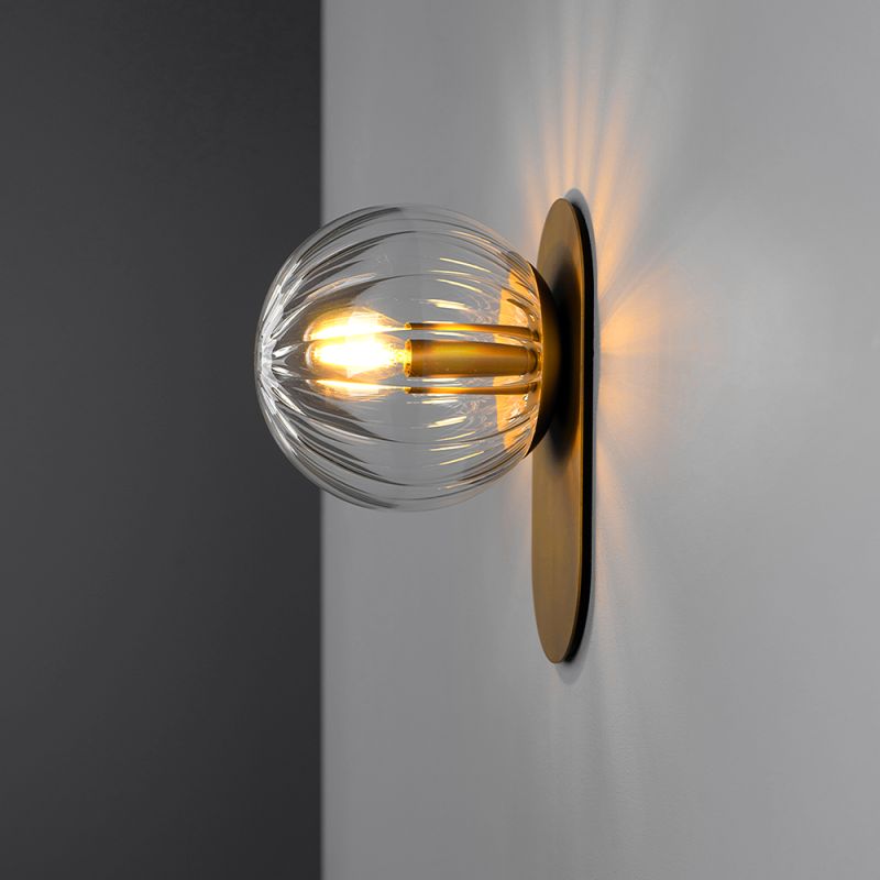 A luxury wall sconce by Schwung with a brushed brass finish and a glamorous detailed clear glass bulb