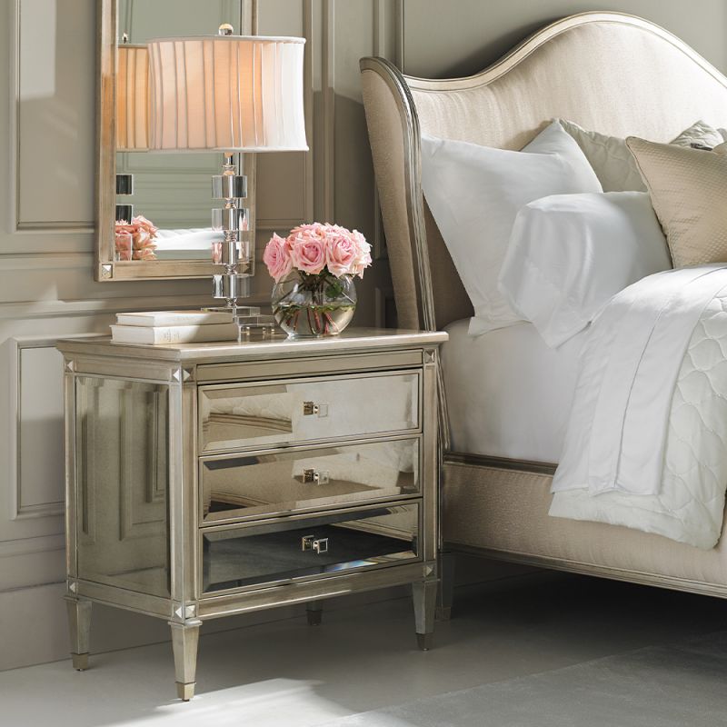 A glamorous bedside table with antique mirrored drawers and a champagne gold finish