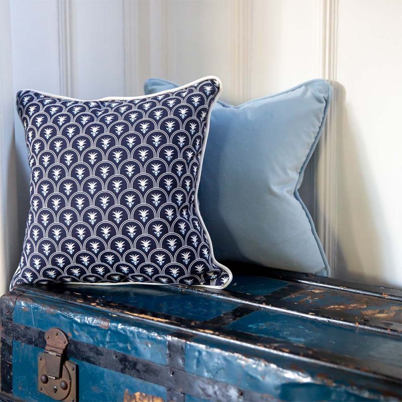 An art deco inspired square cushion with white floral motifs on a dark blue background