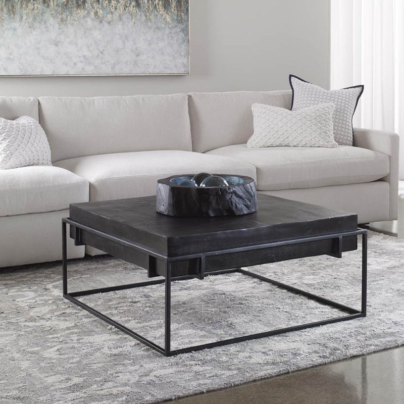 Bold black coffee table with thick surface suspended over minimal black legs