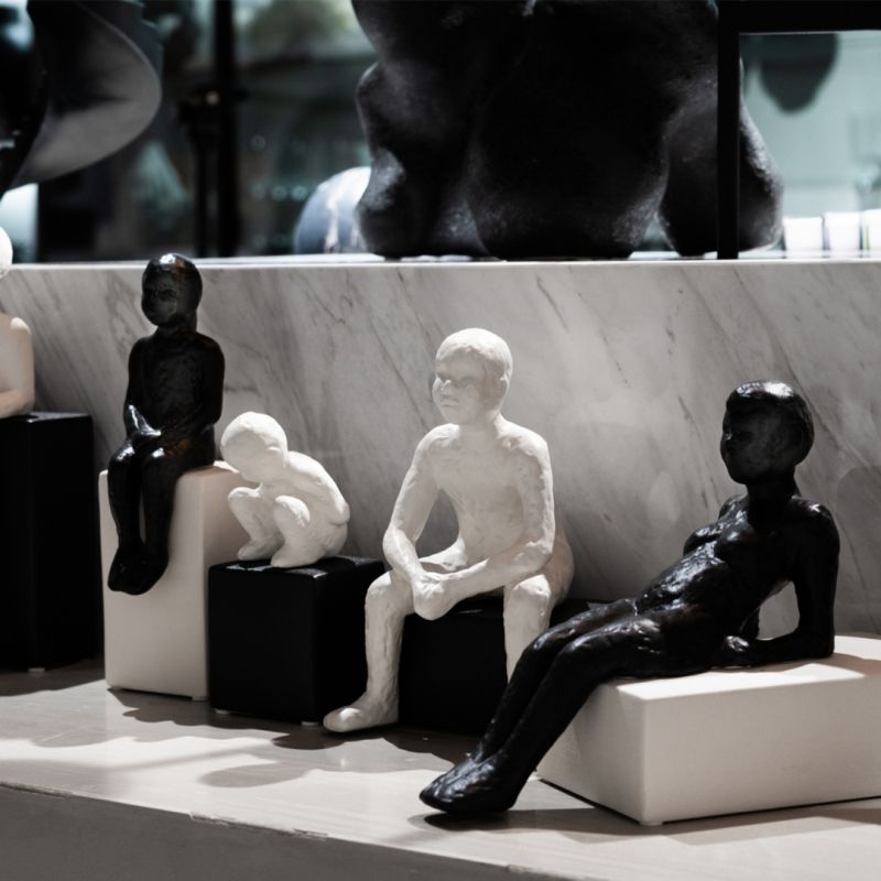 A small ceramic sculpture of a man sat on a black black 