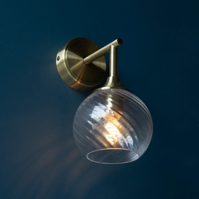 Wall sconce with singular twisted glass globe and brass fixture