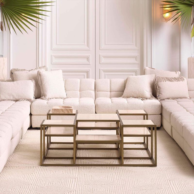 A contemporary coffee table by Eichholtz with a sculptural design featuring a brushed brass finish and travertine table tops