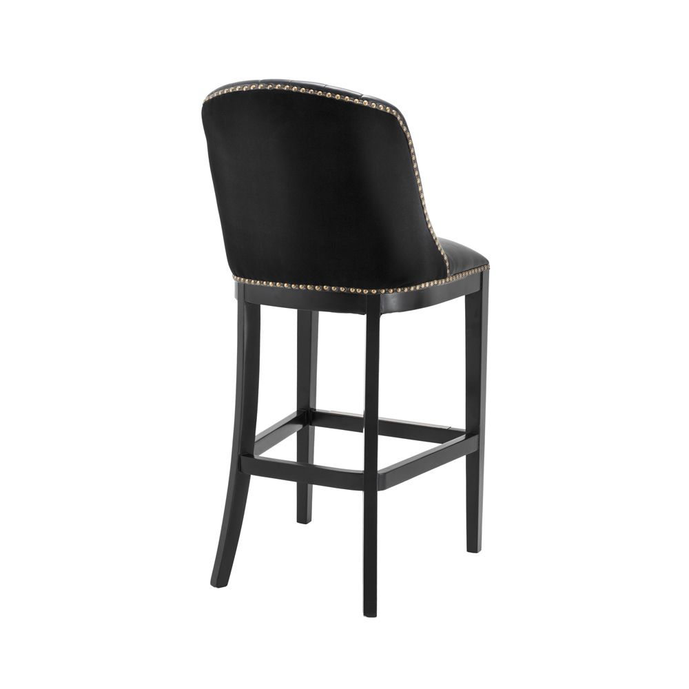 A chic black leather and velvet bar stool with antique brass studding
