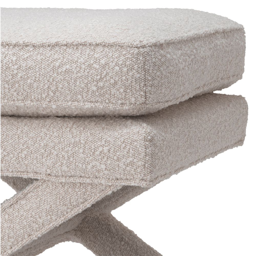 A luxurious boucle cream ottoman with x-shaped legs