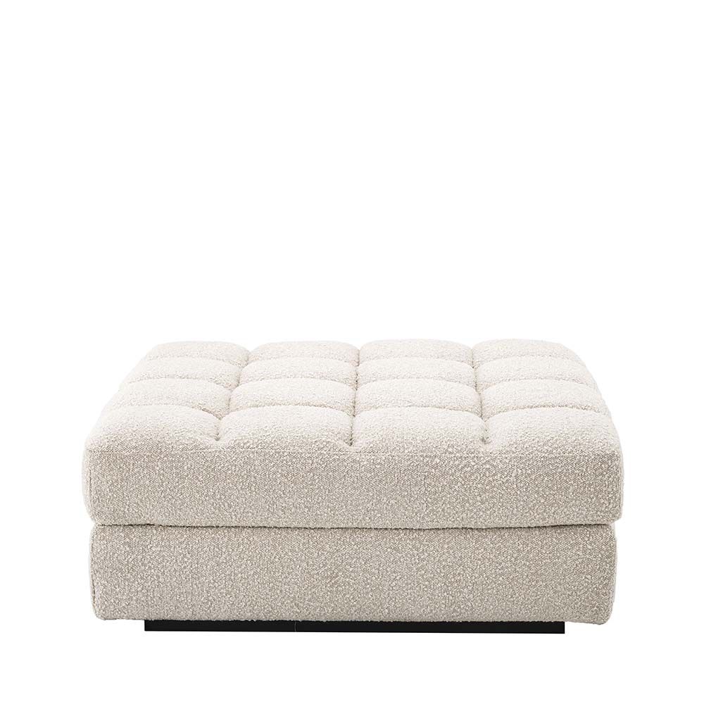 An ottoman upholstered in a boucle cream fabric mounted on a black base.