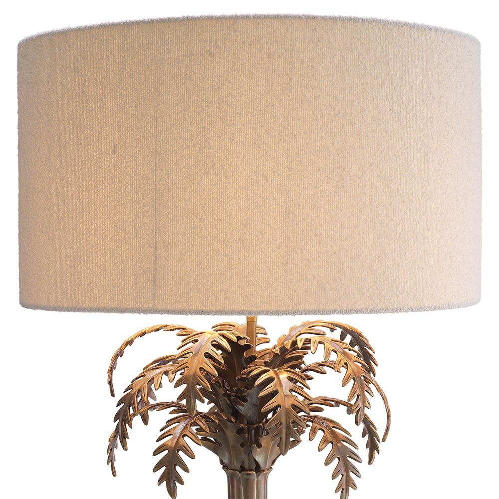 A decorative side lamp by Eichholtz with a boucle cream shade and an Art-Deco tropical tree base with a vintage brass finish