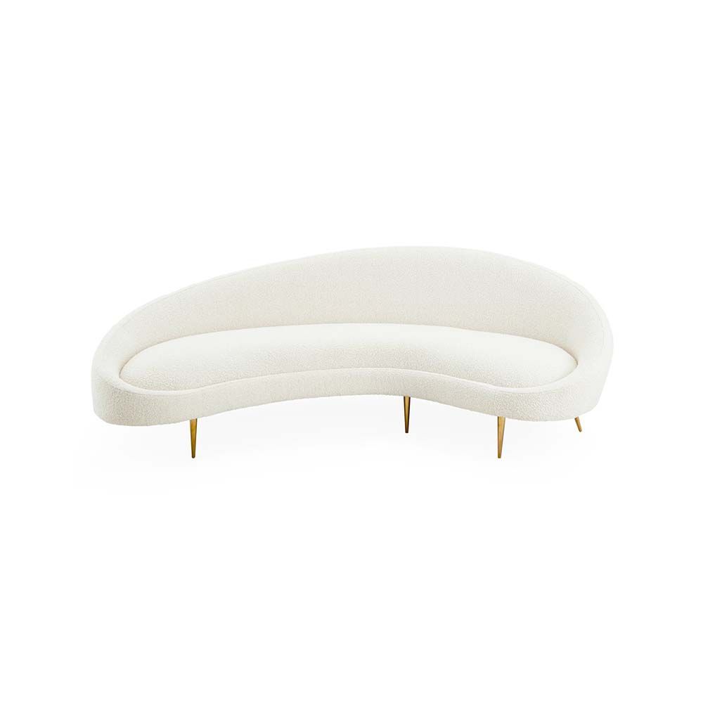 A curved sofa in an upholstered beige boucle fabric with brass legs.