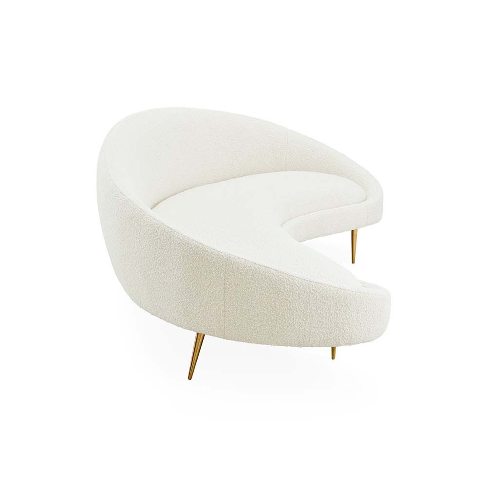 A curved sofa in an upholstered beige boucle fabric with brass legs.