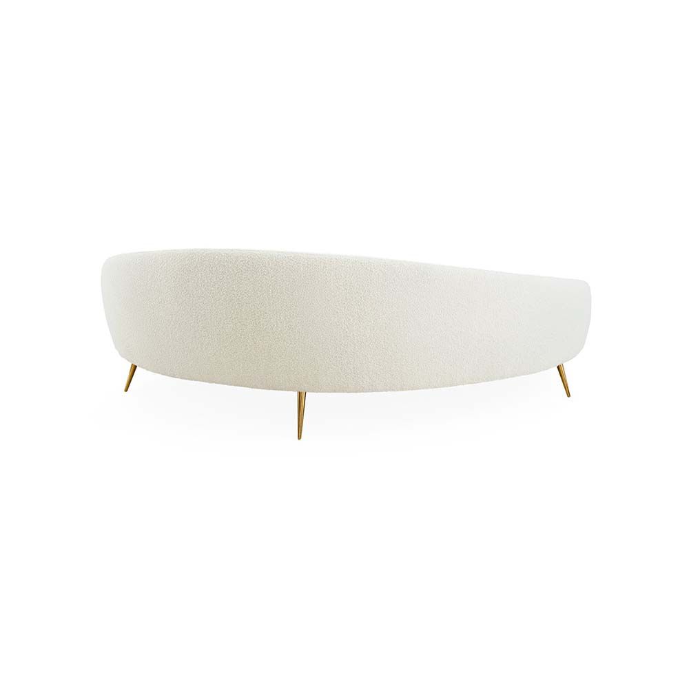 A curved sofa in an upholstered beige boucle fabric with brass legs.