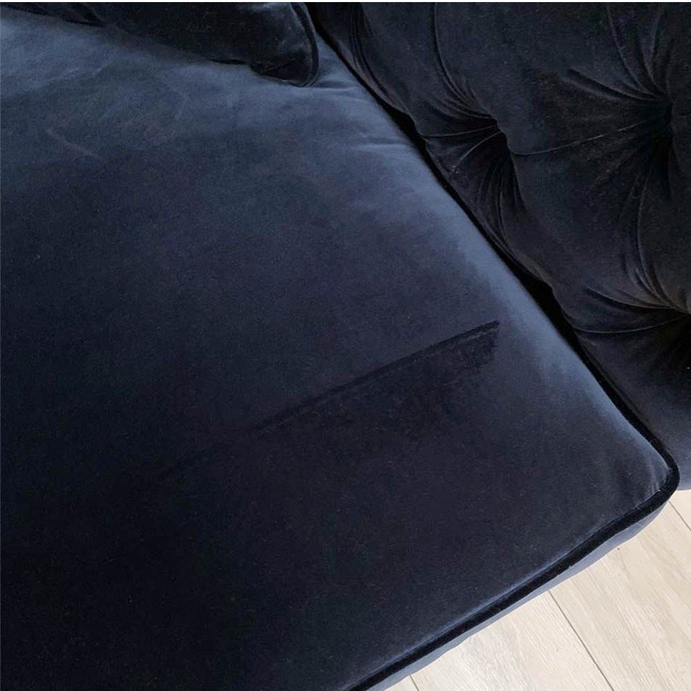 A luxurious sofa with a denim coloured velvet upholstery, deep buttoning and studding 
