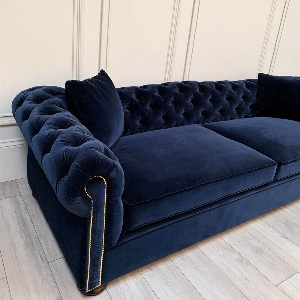 A luxurious sofa with a denim coloured velvet upholstery, deep buttoning and studding 