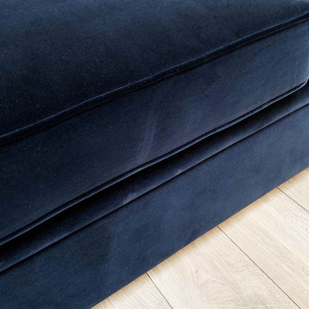 A luxurious sofa with a denim coloured velvet upholstery, deep buttoning and studding 