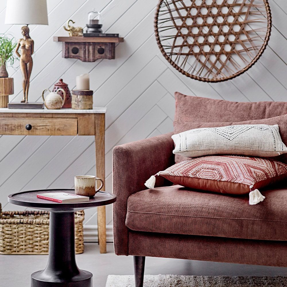 A warm cushion with an intricate embroidered pattern on warm brown linen with added tufted tassel details on each corner