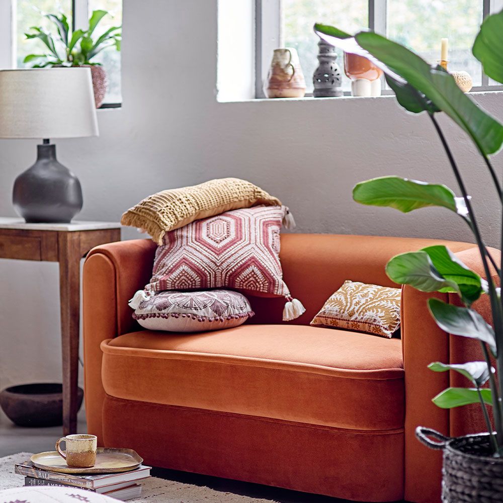 A warm cushion with an intricate embroidered pattern on warm brown linen with added tufted tassel details on each corner