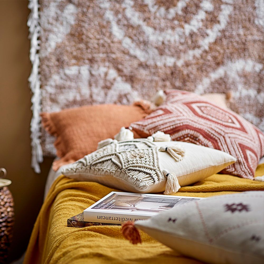 A warm cushion with an intricate embroidered pattern on warm brown linen with added tufted tassel details on each corner