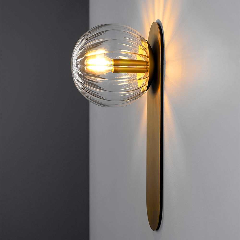 A glamorous wall lamp by Schwung with a brushed brass finish and detailed clear glass bulb
