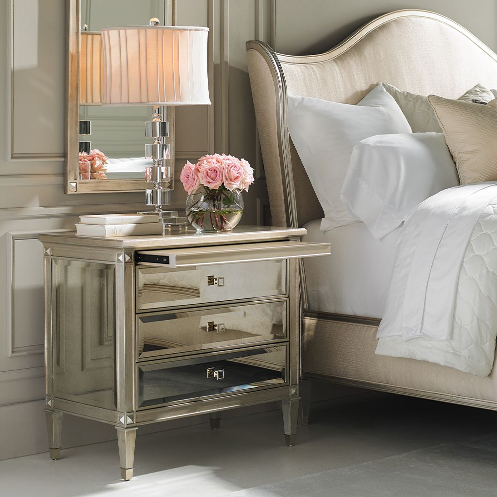 A glamorous bedside table with antique mirrored drawers and a champagne gold finish