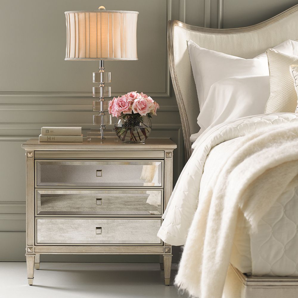 A glamorous bedside table with antique mirrored drawers and a champagne gold finish