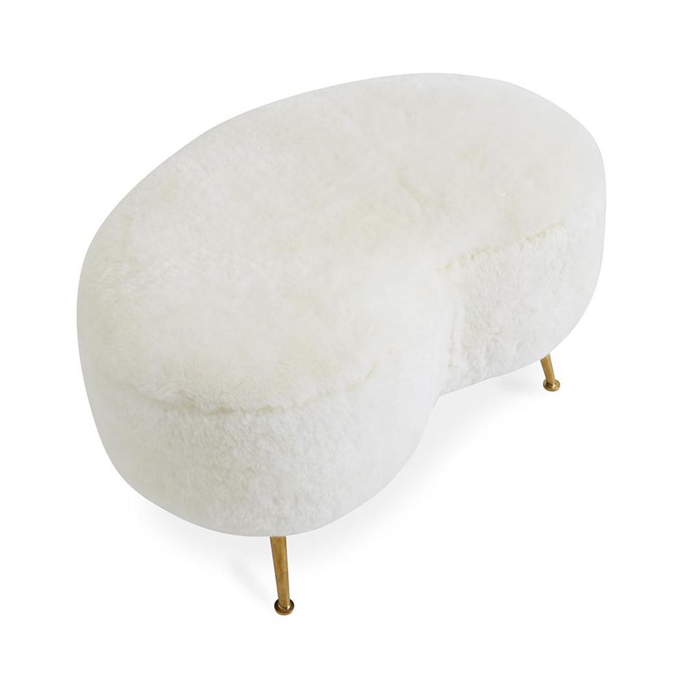 A chic, kidney-shaped shearling ottoman with polished brass legs 