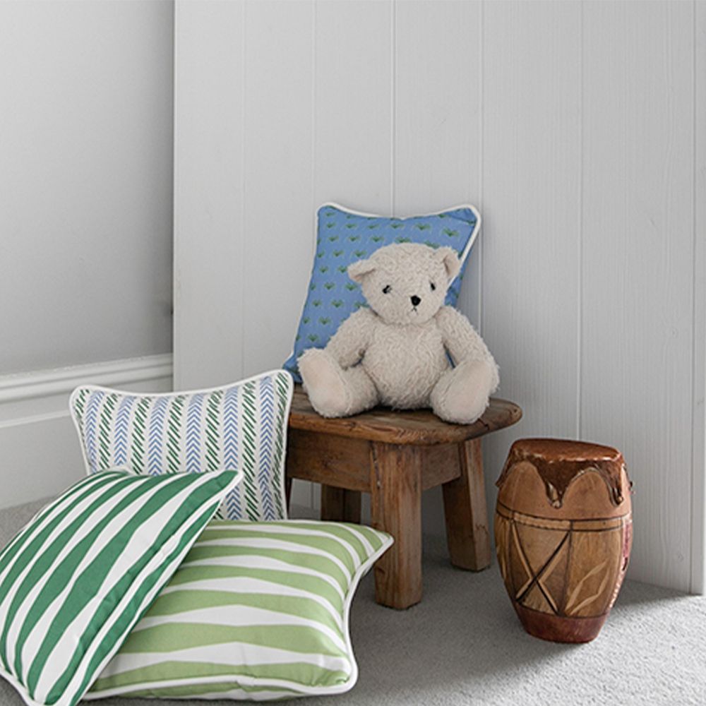 A small green patterned children's cushion with white piping