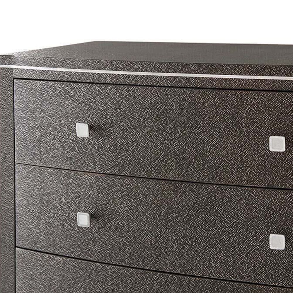 A tall chest of drawers with a luxury design featuring embossed leather, tapered legs and polished nickel adornments