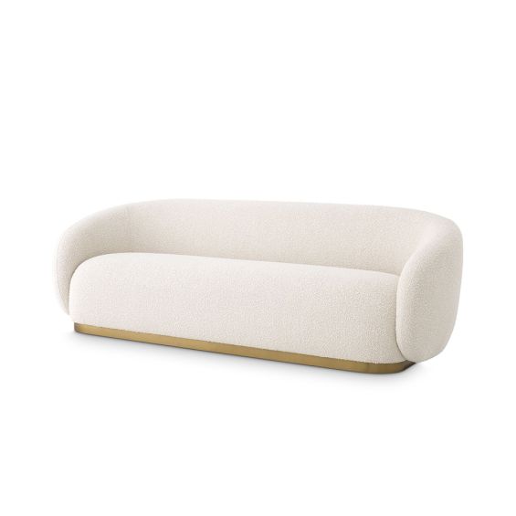 A luxurious cream boucle upholstered sofa with a brushed brass plinth
