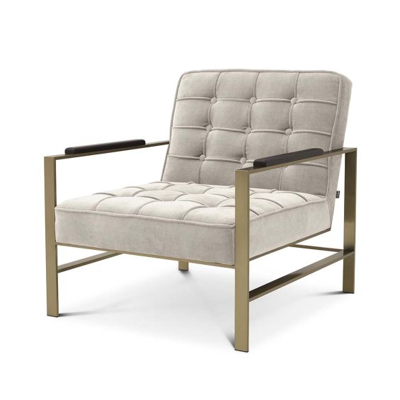 A luxurious natural-toned armchair with a brushed brass frame, defining piping and deep buttoning  