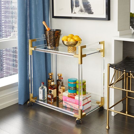 An understated glamorous bar cart made from clear acrylic, brushed brass and glass 