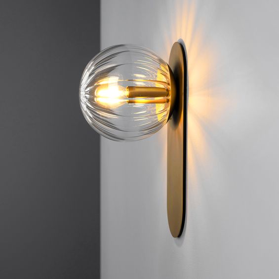 A stunning wall lamp by Schwung with a glamorous brushed brass finish and elegant detailed clear glass bulb
