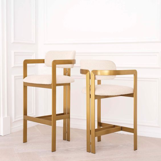 A luxury bar stool by Eichholtz with a boucle seat and brushed brass legs