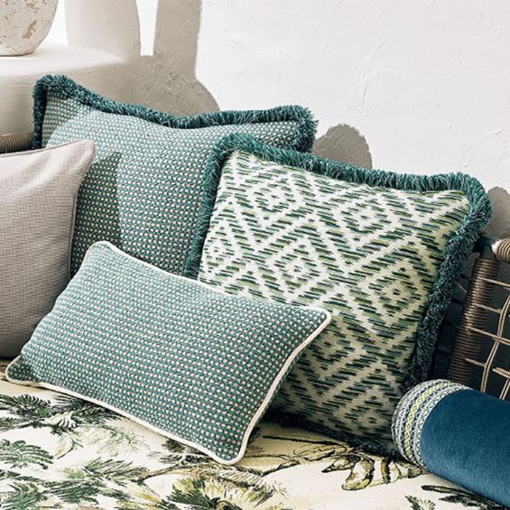 A fringed outdoor cushion with various green hues and chevron details.