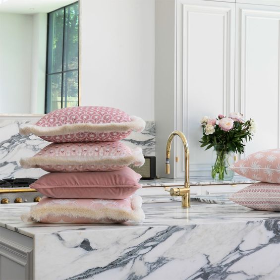 A pastel pink cushion with white floral details and a fringed edge