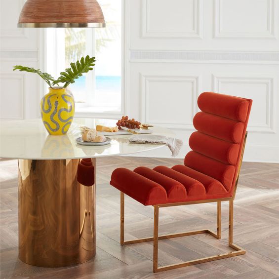 A luxury dining chair by Jonathan Adler with a polished brass base and 70s style red ribbed design