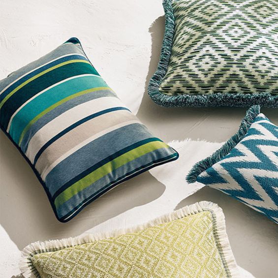 An outdoor, velvet cushion designed with blue and green vertical stripes of different thicknesses.