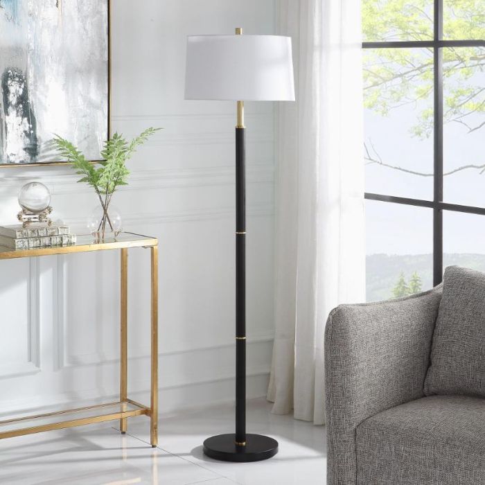 The Troy Floor Lamp, featuring a minimalist design with gold rings along its slender body, is finished with a subtly tapered hardback shade in soft white linen with delicate slubbing, exuding refined elegance.