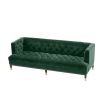 green velvet upholstered deep-buttoned sofa with black legs and brass accents 