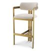 A luxury bar stool by Eichholtz with a boucle seat and brushed brass legs