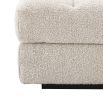 An ottoman upholstered in a boucle cream fabric mounted on a black base.