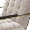 A luxurious natural-toned armchair with a brushed brass frame, defining piping and deep buttoning  